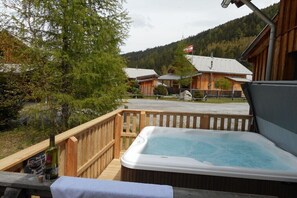 A wooden deck with a hot tub, a bottle of wine, and a glass on a table.