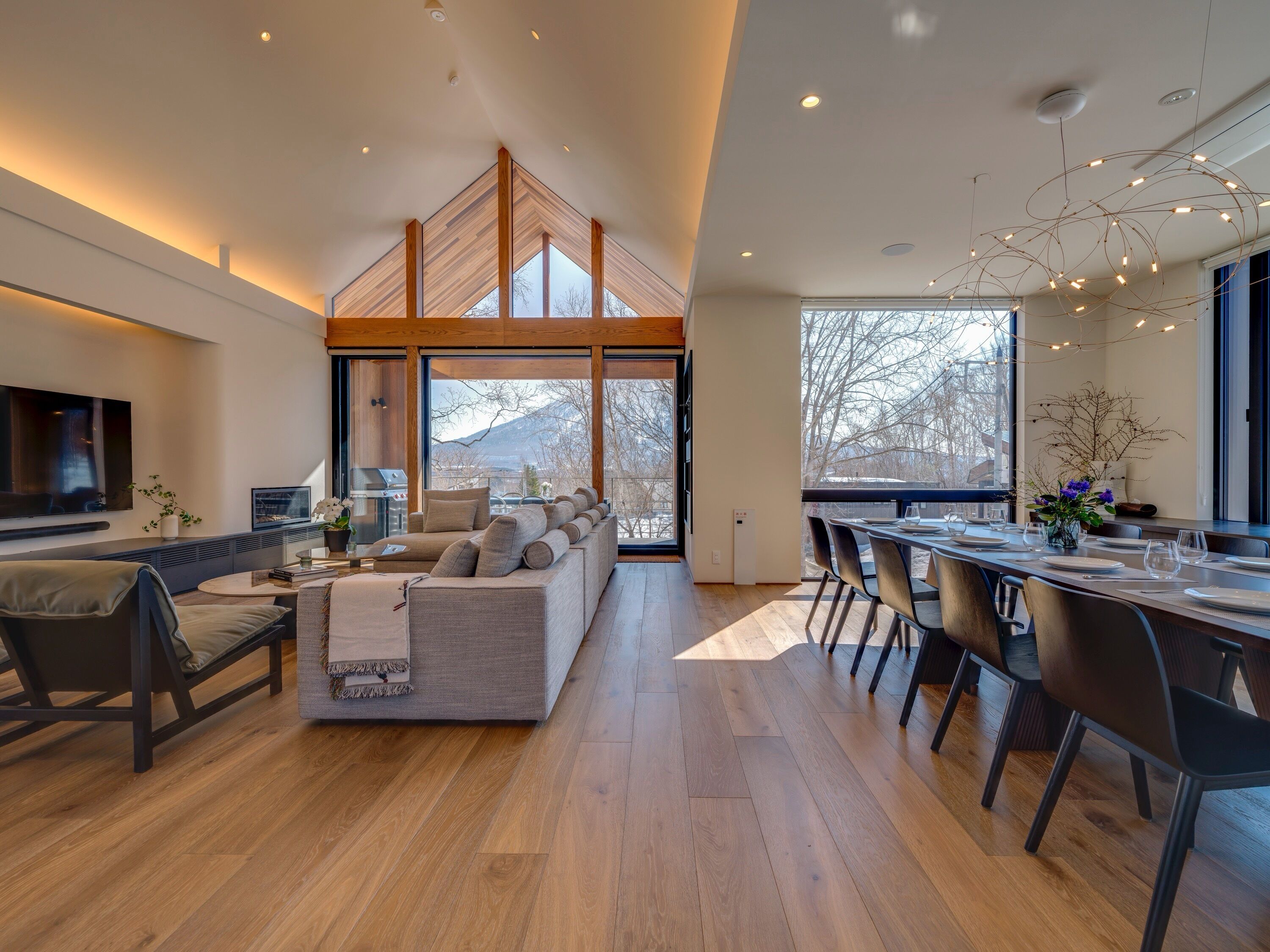 A modern living room with a sofa, dining area, and large windows.