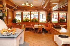 Ein Restaurant mit Holzeinrichtung, mehreren Tischen und großen Fenstern mit Pflanzen.
