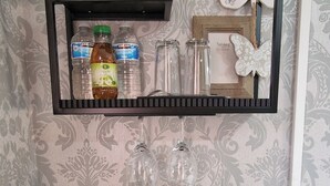 A microwave with a warning label, two white cups on a plate, a framed shelf with decorative items, and a patterned wallpaper background. - Cozy Erith Hideaway - Perfect for Couples (Erith)