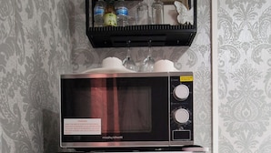 A white Comfee refrigerator with a microwave on top, a black shelf with decorative items, and patterned wallpaper. - Cozy Erith Hideaway - Perfect for Couples (Erith)