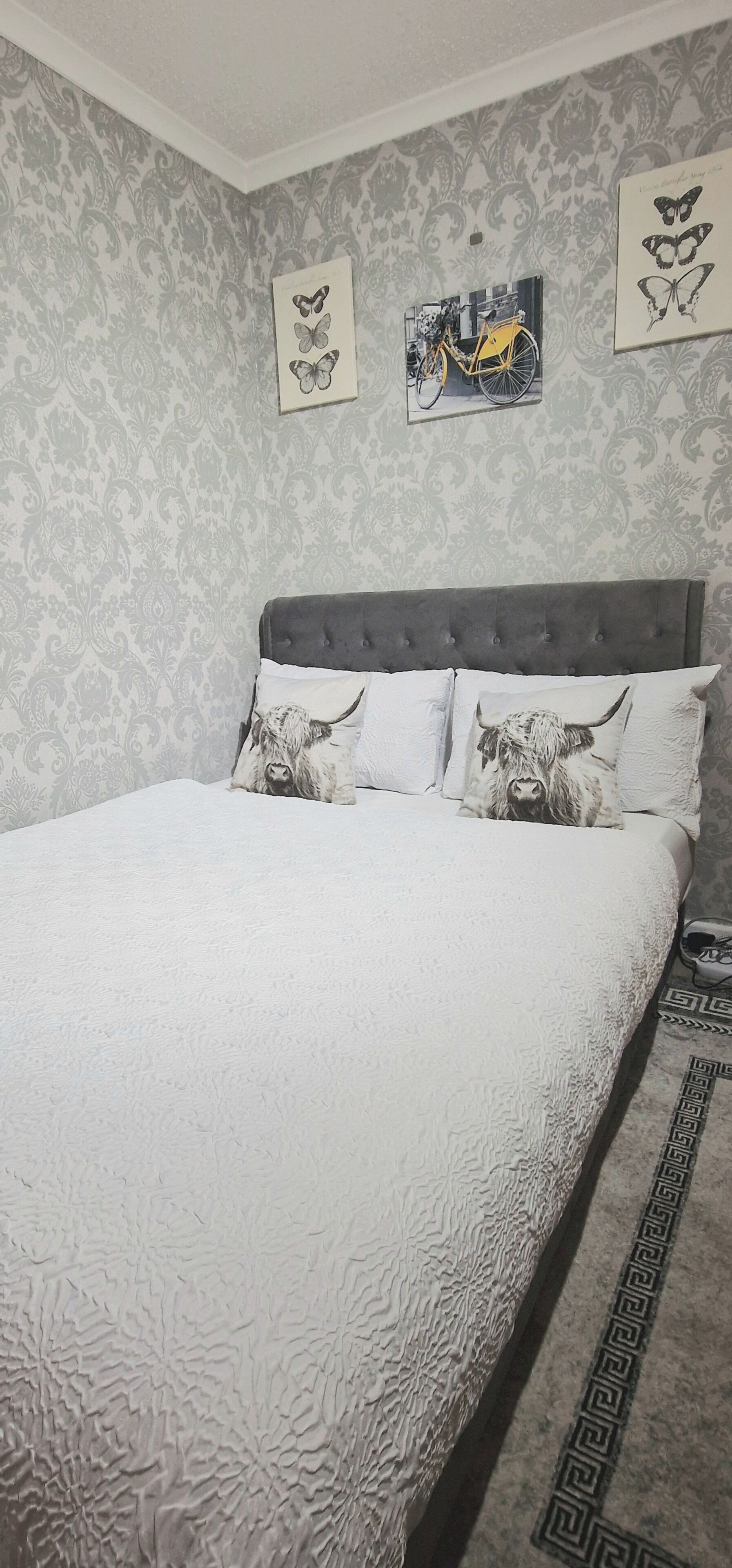 A bedroom with a bed, patterned wallpaper, and decorative wall art.