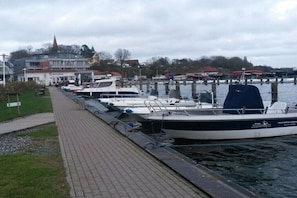 Ein Yachthafen mit vertäuten Booten, einem Weg und Gebäuden im Hintergrund.