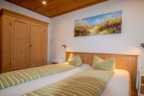 Ein Schlafzimmer mit zwei Betten, einem Holzkopfende, einem Bild mit Strandmotiv und einem Holzschrank.