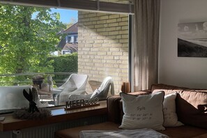 Ein gemütlicher Wohnraum mit Blick auf ein Backsteinhäuschen, einem fenster mit Vorhängen, einem Sofa mit Kissen und einem kleinen Tisch mit Dekoration.