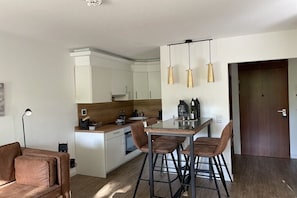 Eine moderne Küche mit weißen Schränken, einer zentralen Kochinsel mit Barhocker, Pendelleuchten und Holzboden.