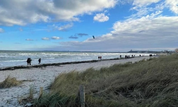 Ein Strand mit einer grasbewachsenen Vordergrundzone, sandigem Ufer und Blick aufs Meer.