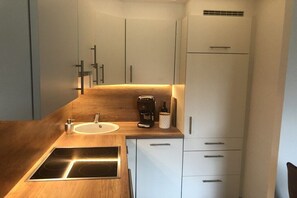 Eine kleine Küche mit eingebautem Herd, einer Kaffeemaschine und einer Weinflasche auf der Arbeitsplatte.