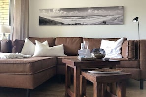 Ein Wohnzimmer mit einem braunen Ledersofa, einem Holztisch und einem großen Landschaftsbild an der Wand.