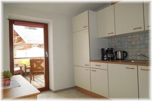 A compact kitchen with white cabinets, a coffee maker, and a dining area with a table and chairs. - Edelweiss Guesthouse in the Ötztal Valley (Sautens)