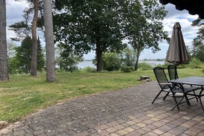 A patio with a table and chairs, a large tree, and a view of a body of water. - Müritzblick No. 11 Ground Floor (Röbel \/ Müritz)