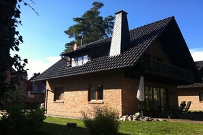 A brick house with a sloped roof, a chimney, and a patio with outdoor furniture. - Müritzblick No. 11 Ground Floor (Röbel \/ Müritz)
