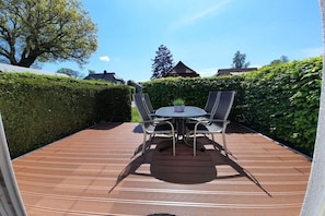 A wooden deck with a round table and four chairs, surrounded by hedges and trees. - Am Wiesengrund House 14 (Ostseebad Prerow)