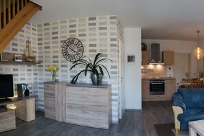A modern living room with a wooden TV stand, a clock, and a potted plant. - Am Wiesengrund House 14 (Ostseebad Prerow)