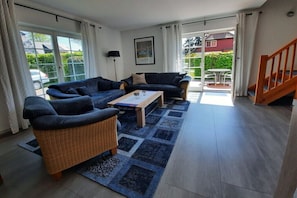 A living room with a sofa, armchair, and coffee table, a staircase, and a view through a glass door. - Am Wiesengrund House 14 (Ostseebad Prerow)