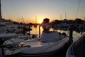 Ein Yachthafen mit vertäuten Booten, ein Sonnenuntergang im Hintergrund und Gebäude entlang des Ufers.