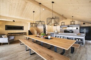 Eine moderne Küche mit Holzbalken, einem langen Esstisch und Pendelleuchten.