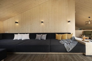 Ein modernes Interieur mit Holzbalkendecke, einer schwarzen Couch mit Kissen und einem kleinen Tisch mit Glasplatte.
