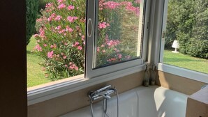 A bathroom with a bathtub, a window, and a view of a garden with pink flowers. - Beautiful contemporary architect-designed home with a pool and garden set amid the garrigue (Nîmes)