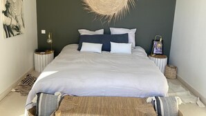 A bedroom with a bed, bedside tables, a wall hanging, and a woven headboard. - Beautiful contemporary architect-designed home with a pool and garden set amid the garrigue (Nîmes)
