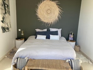 A bedroom with a bed, bedside tables, a wall hanging, and a woven headboard. - Beautiful contemporary architect-designed home with a pool and garden set amid the garrigue (Nîmes)
