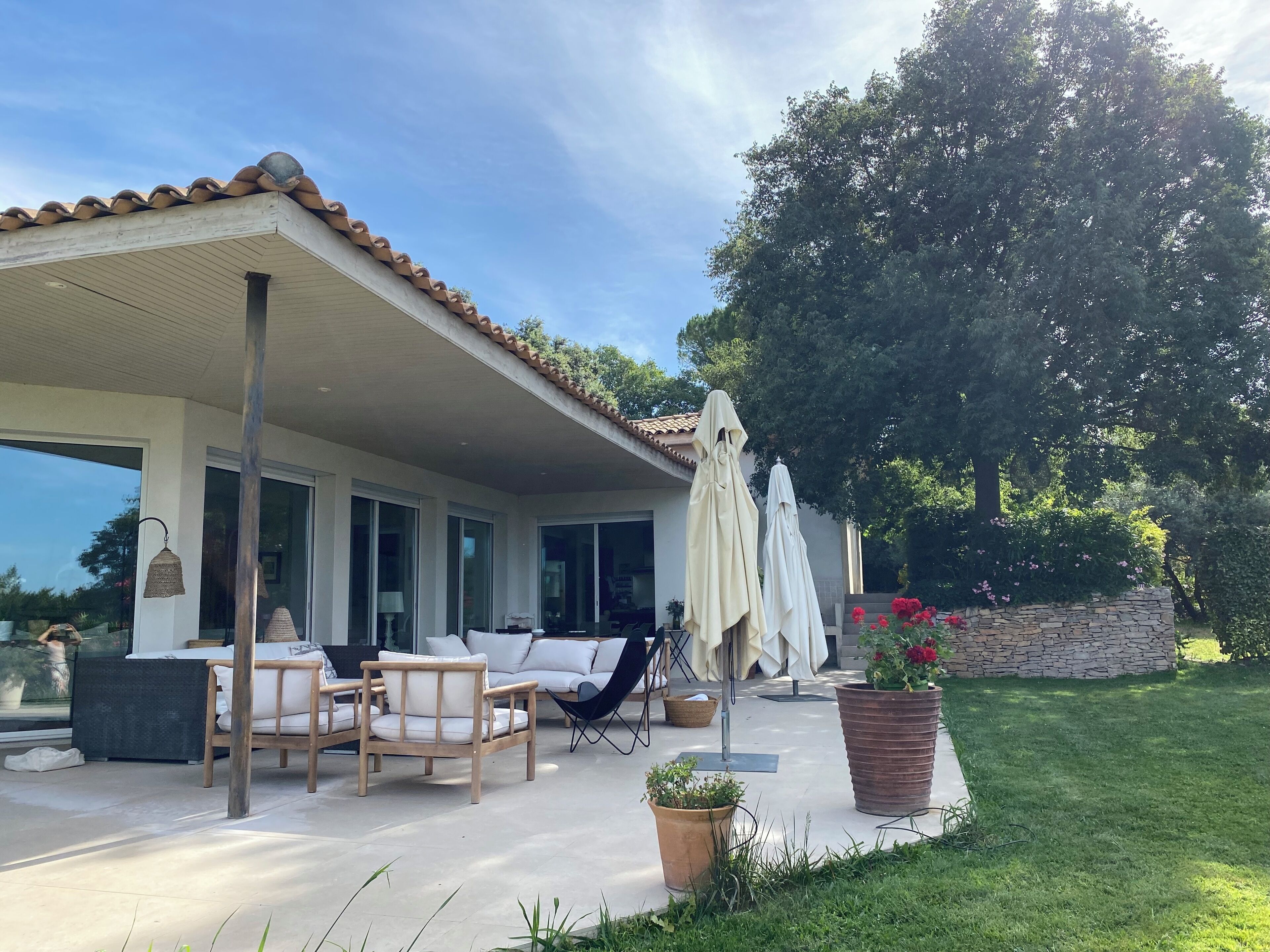 Un patio cubierto con mobiliario exterior, un muro de piedra y un árbol grande.