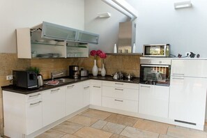 A modern kitchen with white cabinets, a microwave, a stove, and a sink. - Holiday home with 1 bedroom (Harzgerode OT Güntersberge)