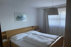 Ein Schlafzimmer mit einem hölzernen Bett, einem Nachttisch, einer Lampe und einem Fenster mit Vorhängen.