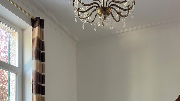 A room with a blue armchair, a mirror, a chandelier, and a wooden staircase. - Le Cantilien (Chantilly)