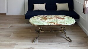A room with a white door, a dark blue sofa with two cushions, and a round table with ornate legs. - Le Cantilien (Chantilly)