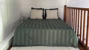 A bedroom with a bed, pillows, a bedside table, a lamp, and a wooden railing. - Le Cantilien (Chantilly)