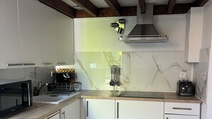 A kitchen with white cabinets, a microwave, a coffee maker, and a stove. - Le Cantilien (Chantilly)