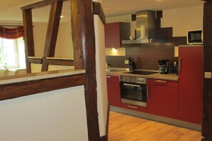 Una cocina con estructura de vigas de madera, estufa, microondas y armarios rojos.