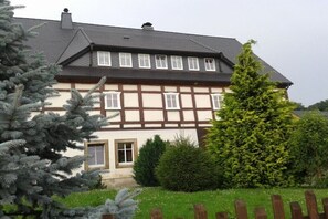 Ein traditionelles Fachwerkhäuschen mit symmetrischer Fassade, einem zentralen Eingang und einem gepflegten Garten mit immergrünen Bäumen.