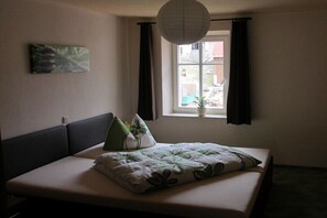 Un dormitorio con cama, ventana con cortinas, lámpara colgante y un cuadro en la pared.