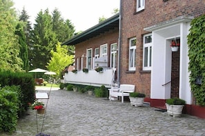 A brick building with a white porch, potted plants, and a cobblestone pathway. - V "Engelwiese" - House of Avalon (Grube)