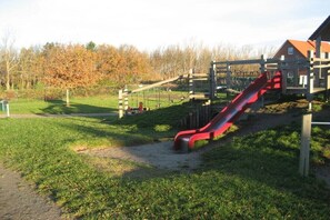 A playground with a red slide, swings, and a wooden structure. - Holiday home with 1 bedroom (Ostseebad Rerik)
