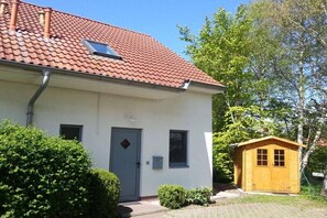 A single-story building with a red-tiled roof, a grey door, and a small attached wooden structure. - Holiday home with 1 bedroom (Ostseebad Rerik)