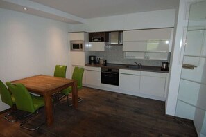 Eine moderne Küche mit weißen Schränken, einer Mikrowelle, einem Herd und einem Essbereich mit Holztisch und grünen Stühlen.