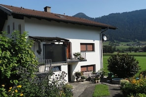 Ein zweigeschossiges Haus mit Balkon, Satellitenschüssel und Garten mit Topfpflanzen.