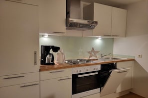 Eine kompakte Küche mit weißen Schränken, einem Backofen, einer Spülmaschine und einer Kaffeemaschine.