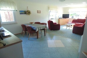 Ein Essbereich mit Tisch und Stühlen, eine Küche mit Fernseher und ein Wohnzimmer mit Sofa und Couchtisch.