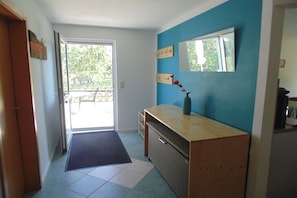 Ein Korridor mit einer Tür zu einem Außenbereich, einer Holzbank, einem kleinen Tisch mit einer Vase und einem an der Wand befestigten Spiegel.