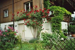 Un edificio con fachada de madera, un jardín con diversas plantas y flores, y una cerca de madera.