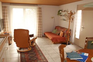 Una sala de estar acogedora con un sofá, una silla, una mesita y un televisor.