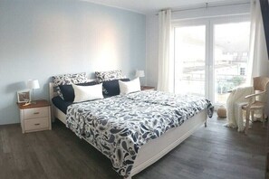 Ein Schlafzimmer mit einem Bett, Nachttischen, einem Sessel und Blick durch ein Fenster.