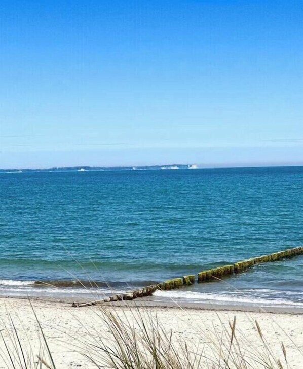 A beach with clear blue water, a sandy shore, and a wooden structure extending into the water. - Beach House Sea Star (Glowe)
