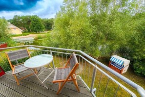 A deck with outdoor furniture, a small table, and a chair, overlooking a body of water and greenery. - Beach House Sea Star (Glowe)