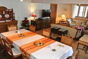 A dining area with a long table set for a meal, a television in the background, and a Christmas tree.