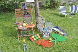 Une collection de raquettes et de balles de tennis est disposée sur une pelouse, avec une chaise en bois et deux chaises longues à rayures.